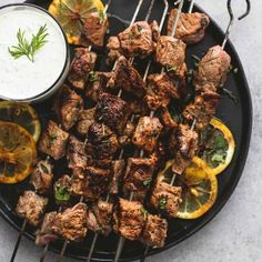 skewered meat and vegetables on a black plate with a small bowl of ranch dressing