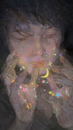 a woman holding her hands up to her face with stars on it and the light coming through her eyes