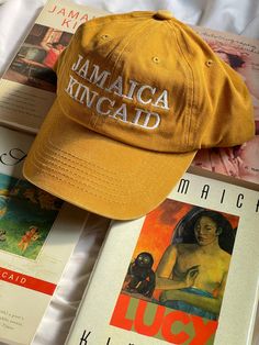 Jamaica Kincaid Womb House Books Hat. Adjustable cotton hat. Mustard yellow color. JAMAICA KINCAID on front, Womb House Books on back. Hat orders are sent every Monday and generally take two weeks to arrive. Yellow Cap For Vacation, Yellow Vacation Cap, Yellow Cotton Dad Hat, Yellow Cotton Curved Brim Dad Hat, Yellow Cotton Dad Hat With Curved Brim, Yellow Cotton Dad Hat, One Size Fits Most, Yellow Cotton Hat (one Size Fits Most), Yellow Wide Brim Cotton Hat, Yellow Cotton Hat With Curved Brim