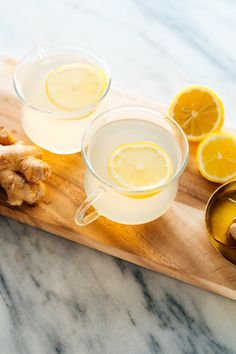 two glasses of lemonade and ginger tea on a cutting board with sliced lemons