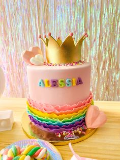 there is a pink cake with rainbow icing and a crown on top