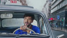 a man sitting in the driver's seat of a taxi cab driving down a street