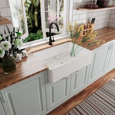 a white kitchen sink sitting under a window next to a counter with flowers in it