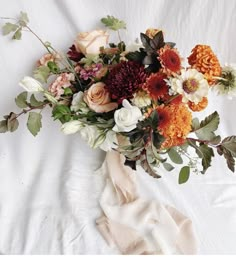 a bouquet of flowers is laying on a white sheet, with leaves and branches around it