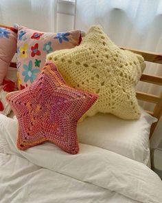 three crocheted stars sit on top of a bed with white sheets and pillows