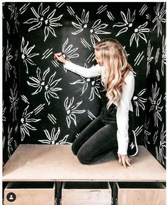 a woman sitting on top of a wooden bench in front of a black and white wall