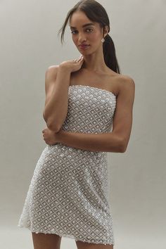 a woman in a short white dress posing for the camera with her hand on her chin