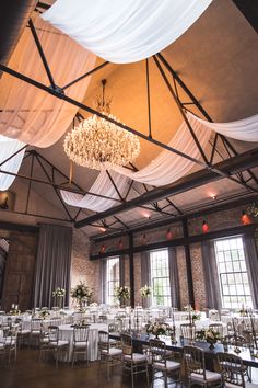 an indoor wedding venue with chandeliers and white drapes hanging from the ceiling