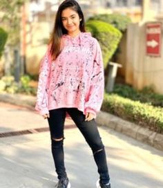 a woman standing in the street wearing black ripped jeans and a pink top with an animal print