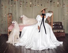 a woman in a white dress and hat sitting on a bed with two dogs next to her