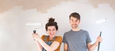 a man and woman standing next to each other holding paint rollers