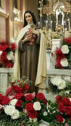 a statue of the virgin mary with flowers in front of her and candles behind it