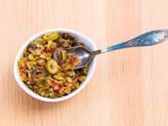 a white bowl filled with food sitting on top of a wooden table next to a spoon