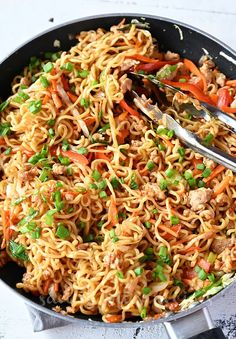 a skillet filled with noodles and vegetables on top of a white countertop next to a fork