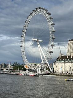 a large ferris wheel sitting on the side of a river next to tall buildings and water