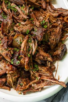 a white plate topped with shredded meat and garnished with parsley on top