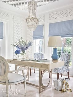 a white room with blue and white chairs, a chandelier and a desk