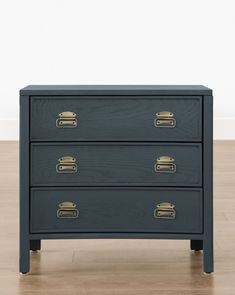 a black chest of drawers with brass handles on the top and bottom, against a white wall