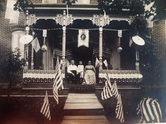 an old black and white photo of people sitting on a porch with american flags around them