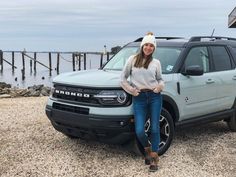 a woman standing in front of a truck by the water with her hands on her hips