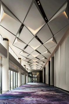 an empty hallway with purple carpeting and columns on both sides, along with large windows