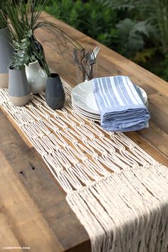 a wooden table topped with plates and vases filled with plants next to a white plate