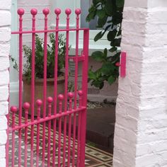 a pink gate is open on the side of a white building with potted plants