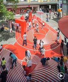 many people are walking around on the red and white striped surface in an urban area