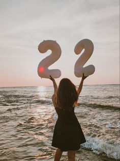 a woman standing on the beach holding up two large numbers