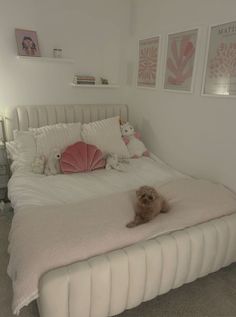 a small dog laying on top of a white bed in a room with pink and white decor