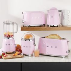 a pink blender sitting on top of a counter next to toasters and fruit