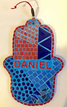 a blue and red hamsa hanging from a wall with the word daniel on it