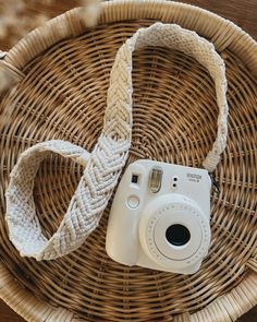 a white camera sitting on top of a wicker basket next to a woven strap