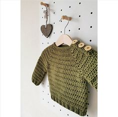 a green knitted sweater hanging on the wall next to a pair of wooden pegs