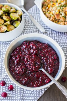 a bowl of cranberry sauce next to two bowls of brussel sprouts