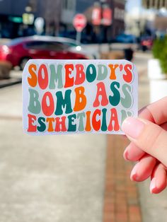 someone holding up a sticker that says somebody's bombass nurse