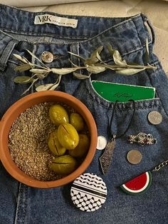 a bowl filled with green olives sitting on top of a pair of jeans