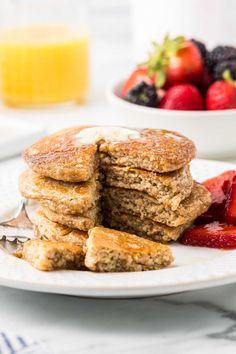 a stack of pancakes with strawberries on the side and a bowl of fruit in the background