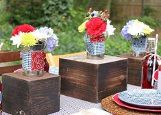 three vases with flowers sit on top of wooden blocks at a table set for an outdoor party