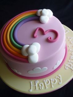 a birthday cake with rainbows and clouds on it's top is for a girl