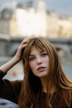 a woman with long brown hair and blue eyes posing for the camera in front of a cityscape