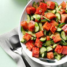 a white bowl filled with cucumber and tomato salad on top of a table