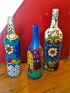 three colorful painted vases sitting on top of a wooden table next to a red wall