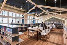 people are sitting at tables in the middle of a library with lots of bookshelves