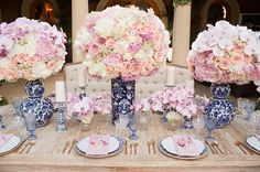 pink and white flowers in blue vases on a table with place settings for dinner