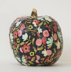 a painted pumpkin sitting on top of a white table next to a black and pink flowered apple