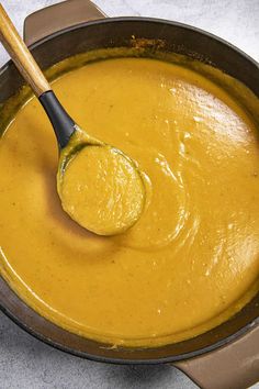 a wooden spoon in a pot filled with yellow liquid and sauce on a table top