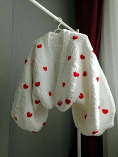 a white sweater with red hearts on it hanging from a hook