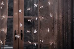 an open window with white stars on the curtain and light shining through it, in front of a dark background