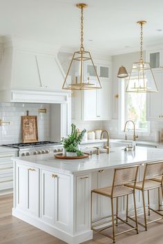 a white kitchen with gold accents and pendant lights hanging from the ceiling over the island